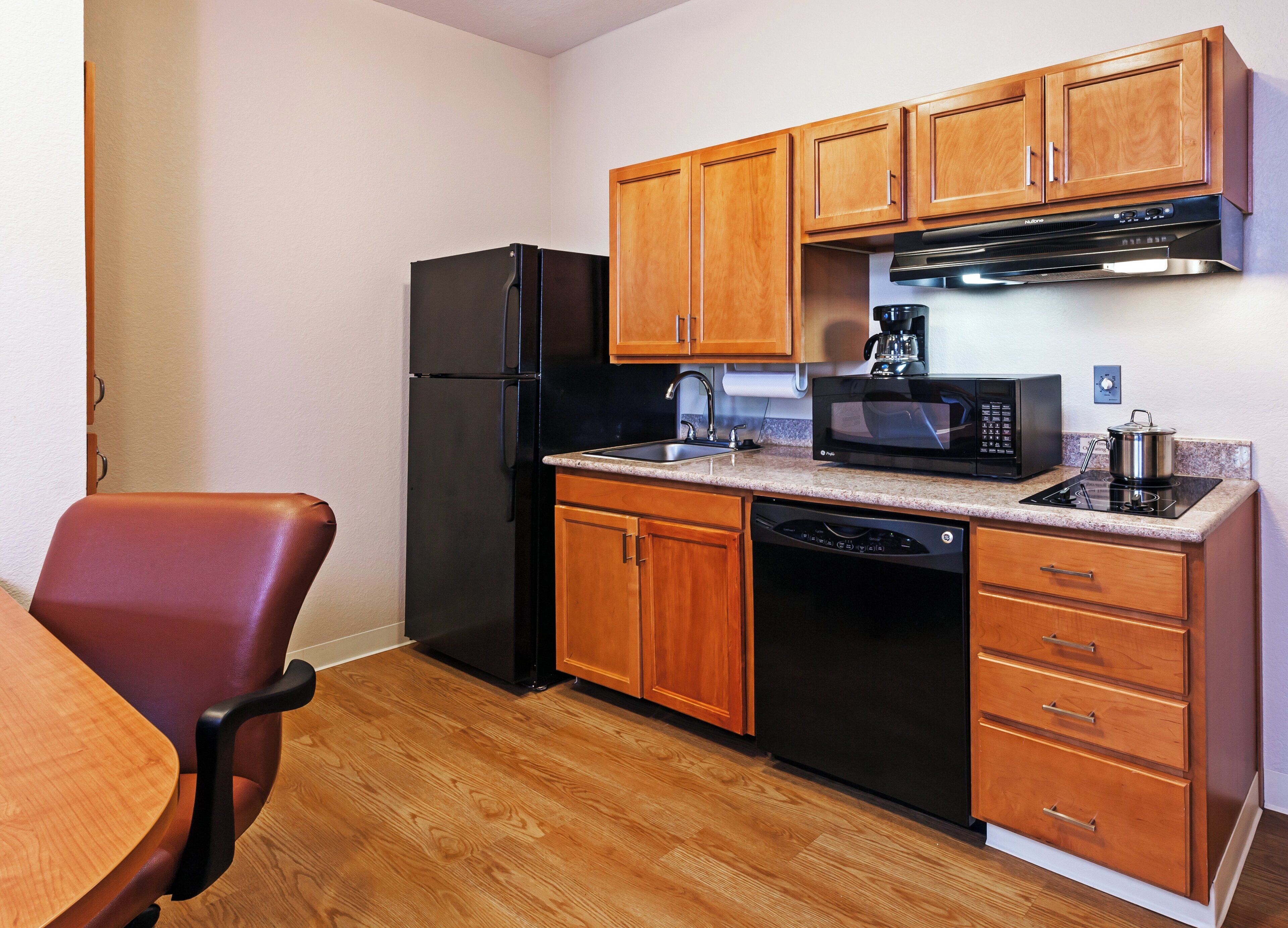 A compact kitchen with wooden cabinets, a black refrigerator, a microwave, and a dishwasher.