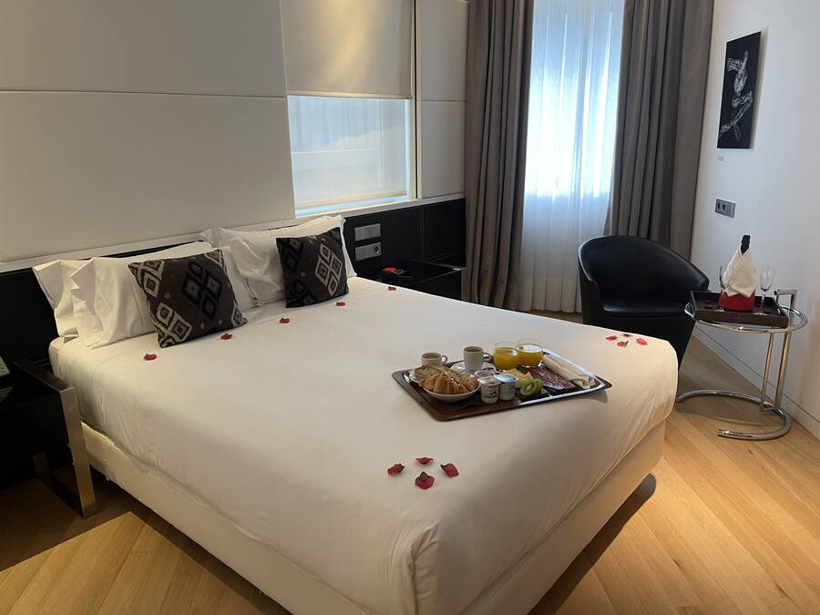 Une chambre d’hôtel avec un lit soigneusement fait, un plateau de petit-déjeuner et une chaise.