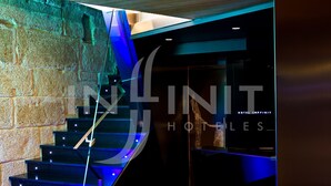 A modern staircase with glass railings and blue lighting, leading to a reception area with a sign for Hotel Infiniti. - Hotel Inffinit (Vigo)
