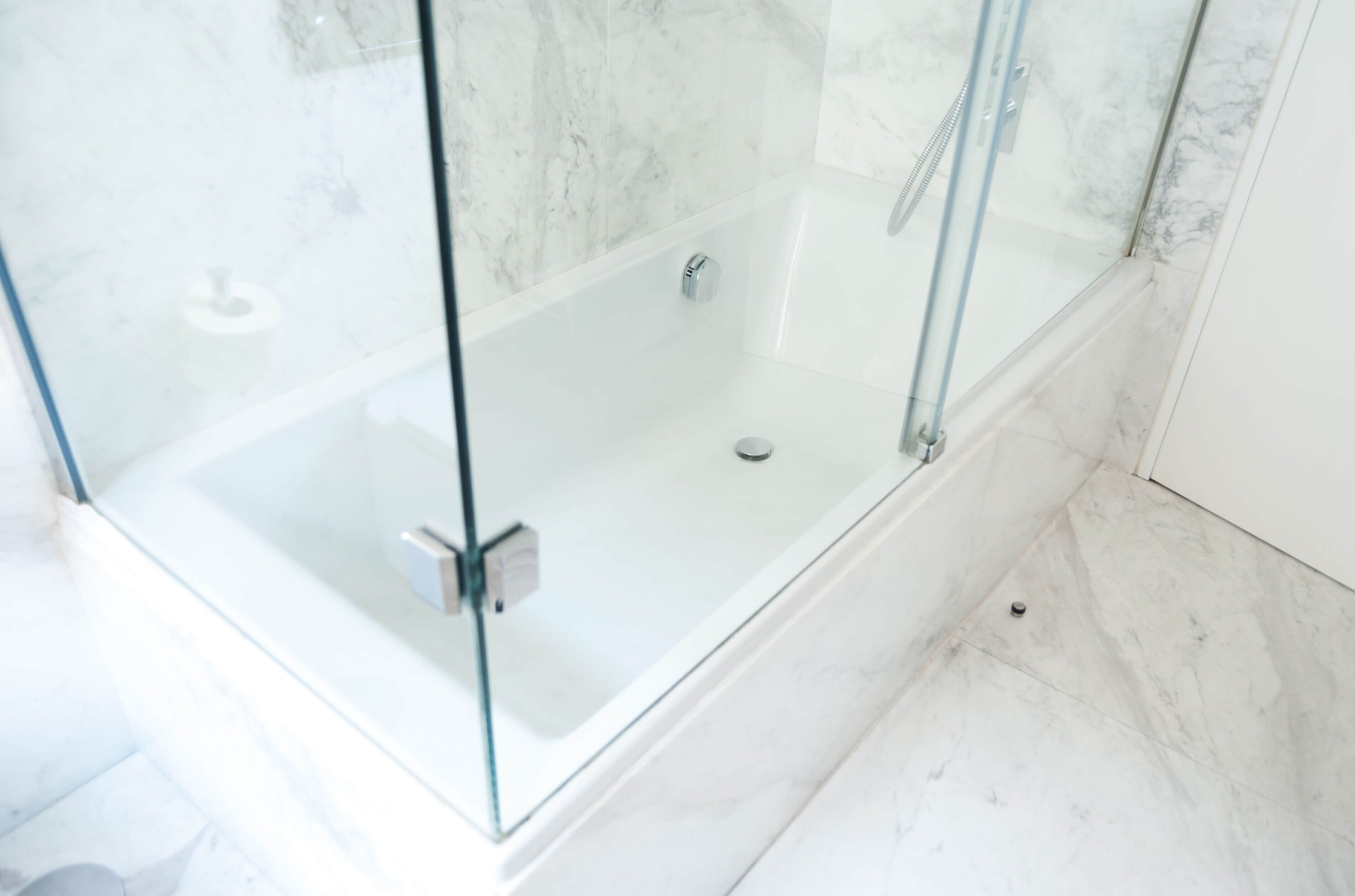 Een douche met glazen wanden en een marmeren vloer.