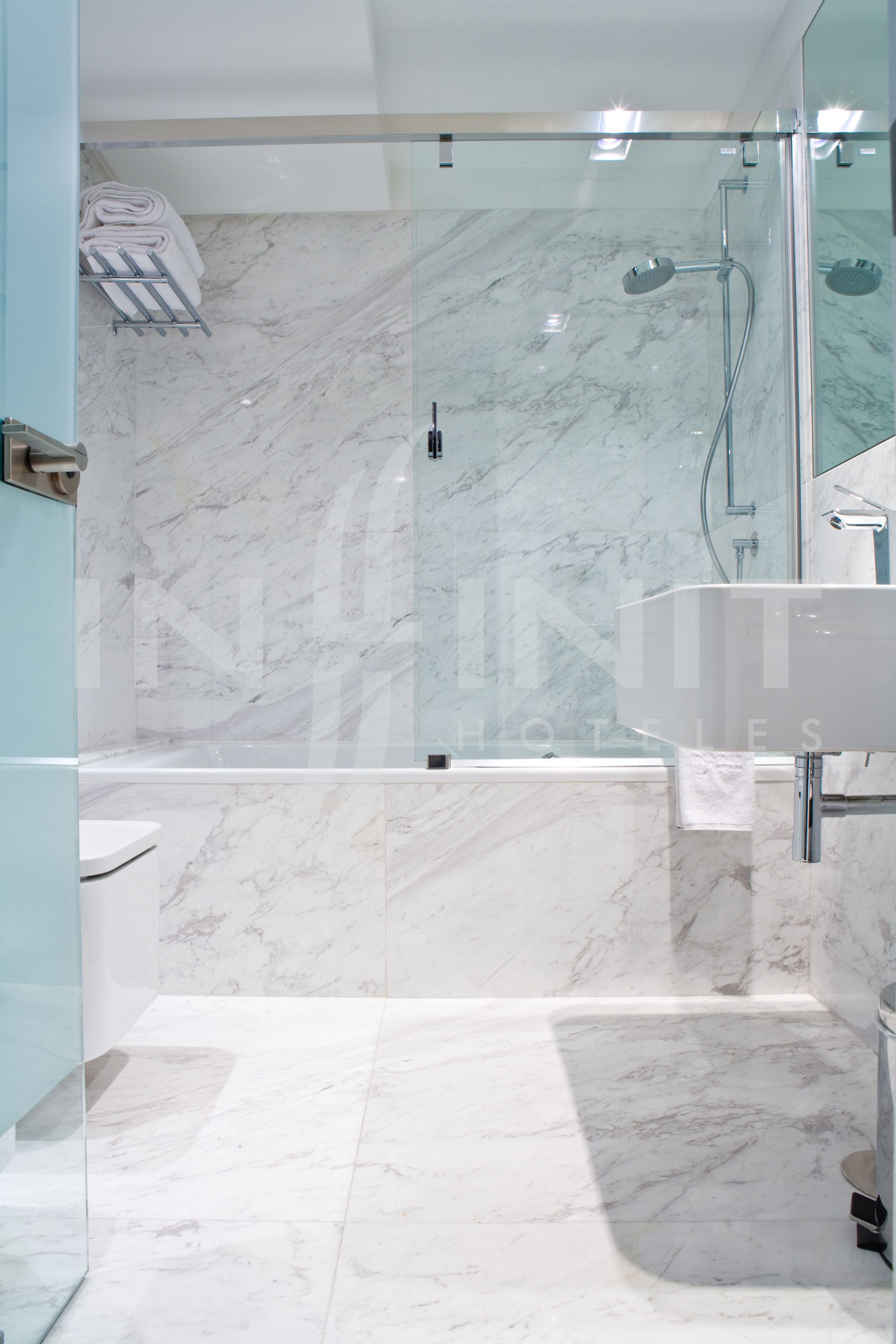 Un baño moderno con ducha envuelta en vidrio, un lavabo blanco y suelo de mármol.