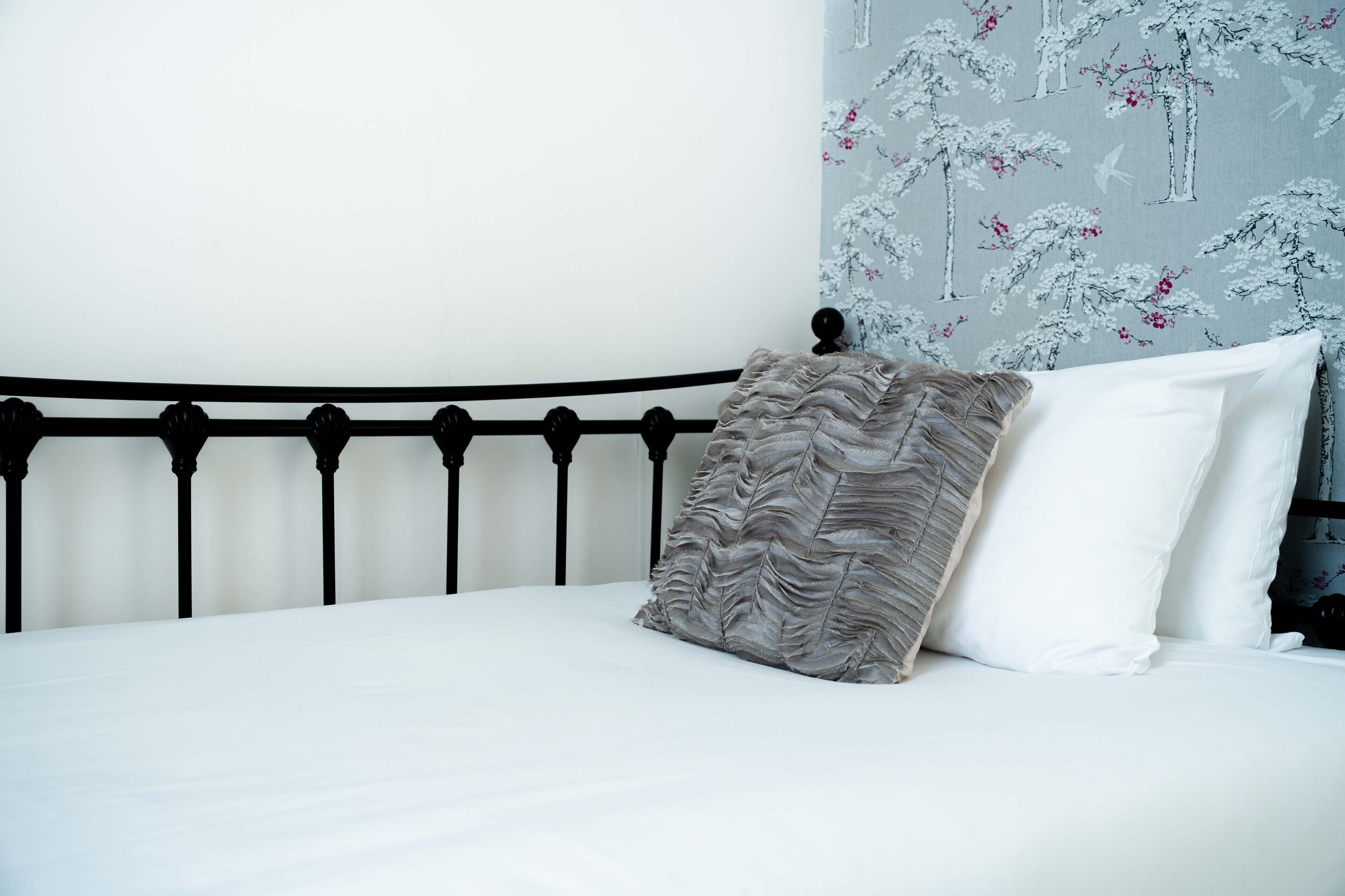 A neatly made bed with a black metal headboard, white bedding, and a patterned pillow.