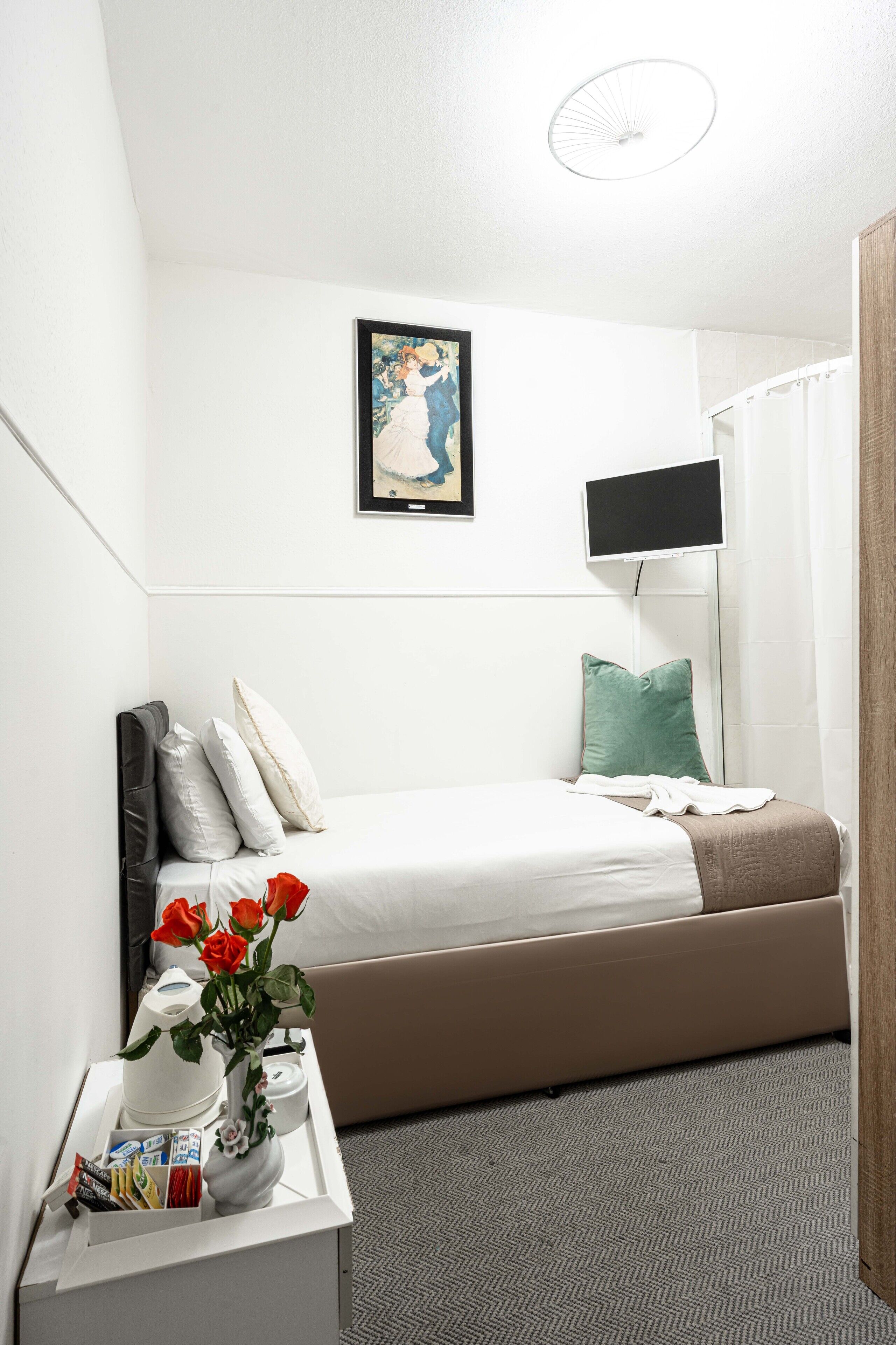 A hotel room with a bed, a bedside table with a vase of flowers, a flat-screen TV, and a painting on the wall.