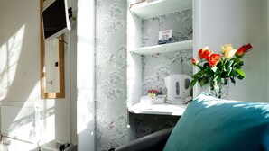 A room with a radiator, a mirror, a shelf with a kettle, and a vase with flowers. - Lancaster Court Hotel (London)