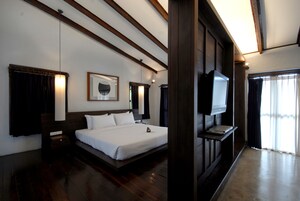 A hotel room with a large bed, a flat-screen TV mounted on the wall, and a wooden ceiling.