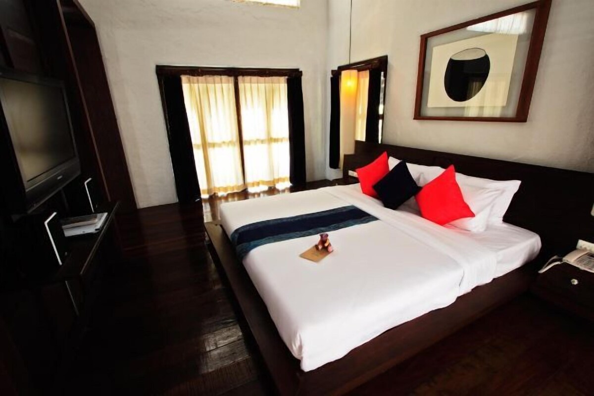A hotel room with a large bed, a TV, and a window with curtains.