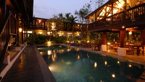 A poolside area with a wooden deck, lounge chairs, and a restaurant with outdoor seating. - Banthai Village (Chiang Mai)