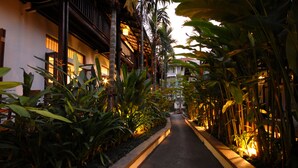 A narrow pathway flanked by lush tropical plants and traditional wooden buildings with warm lighting. - Banthai Village (Chiang Mai)