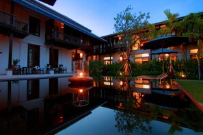 Een hotel met een zwembad, terras en een goed verlichte tuin.