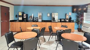 A clean, well-lit restaurant with a blue accent wall, a counter with coffee machines, and several tables and chairs. - Days Inn by Wyndham Lumberton (Lumberton)