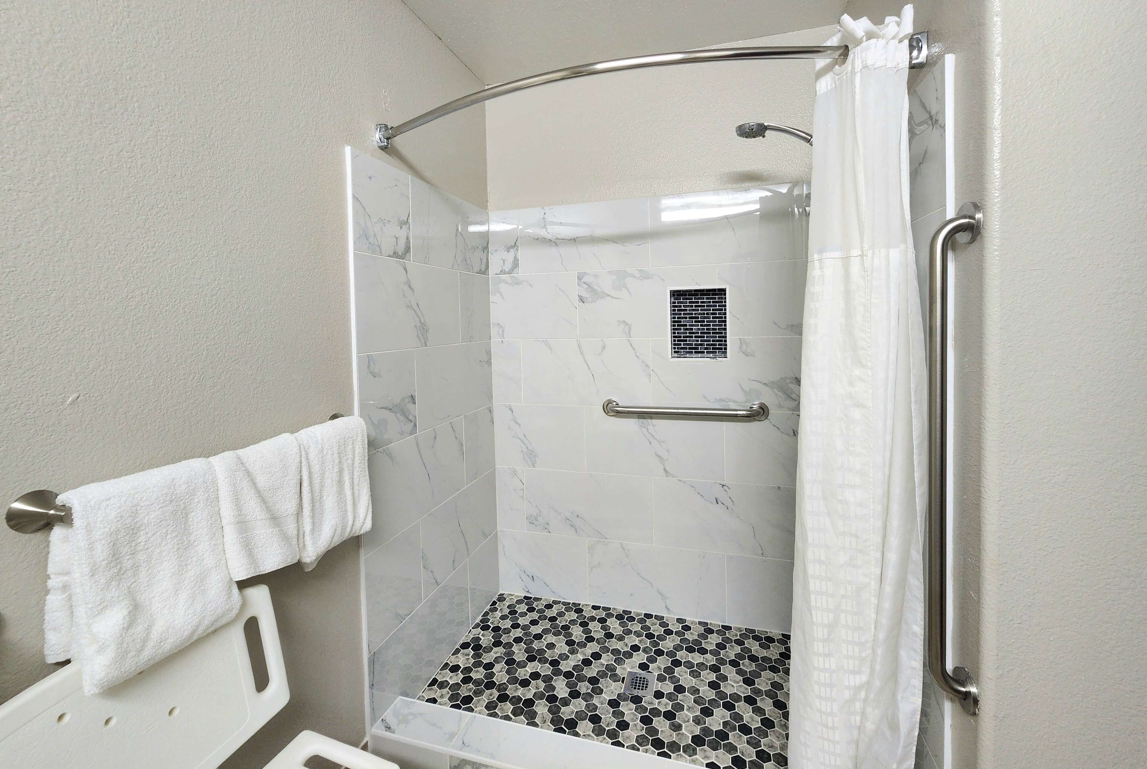 A shower with a white towel hanging on a rack, a glass door, and a tiled floor with a hexagonal pattern.