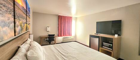 A hotel room with a large bed, a desk with a chair, a television, and a window with curtains.