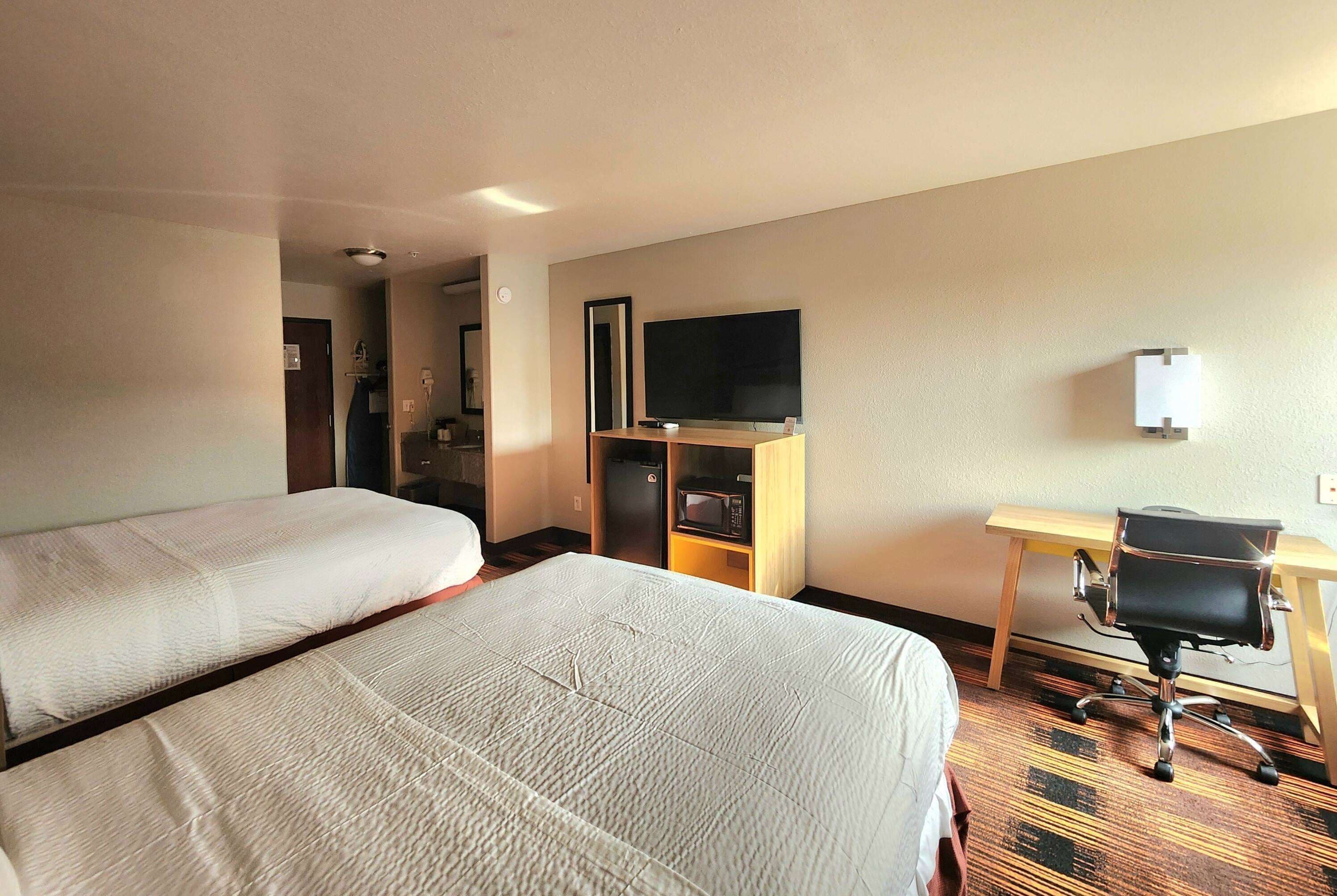 Habitación de hotel con dos camas, un escritorio, una silla, un televisor y un microondas.