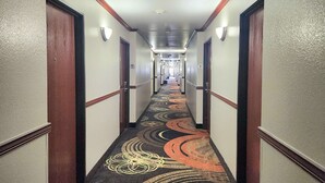 A hotel hallway with a carpeted floor, wooden doors, and wall-mounted light fixtures. - Days Inn by Wyndham Lumberton (Lumberton)