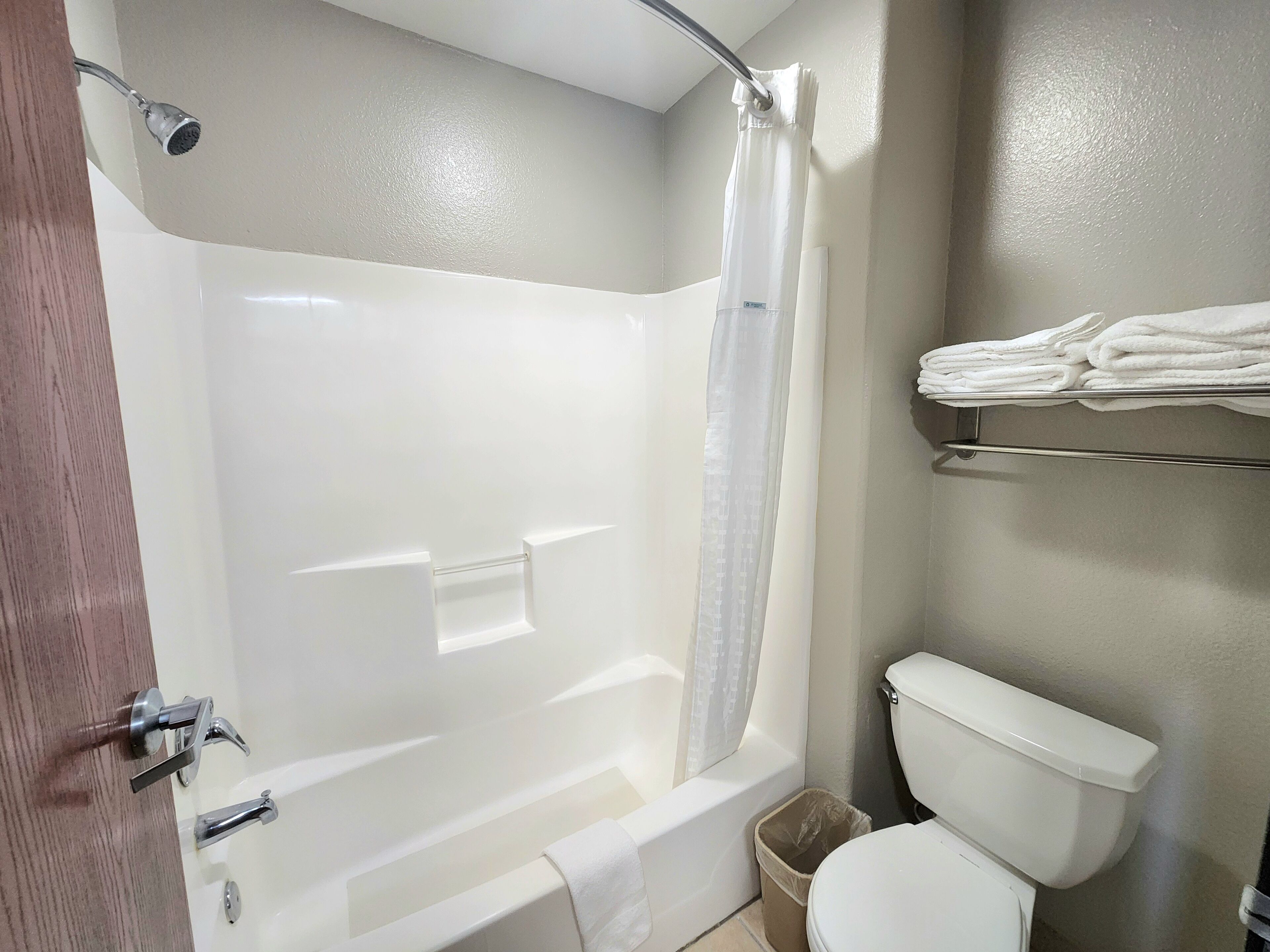 A bathroom with a bathtub, toilet, and a shelf with folded towels.