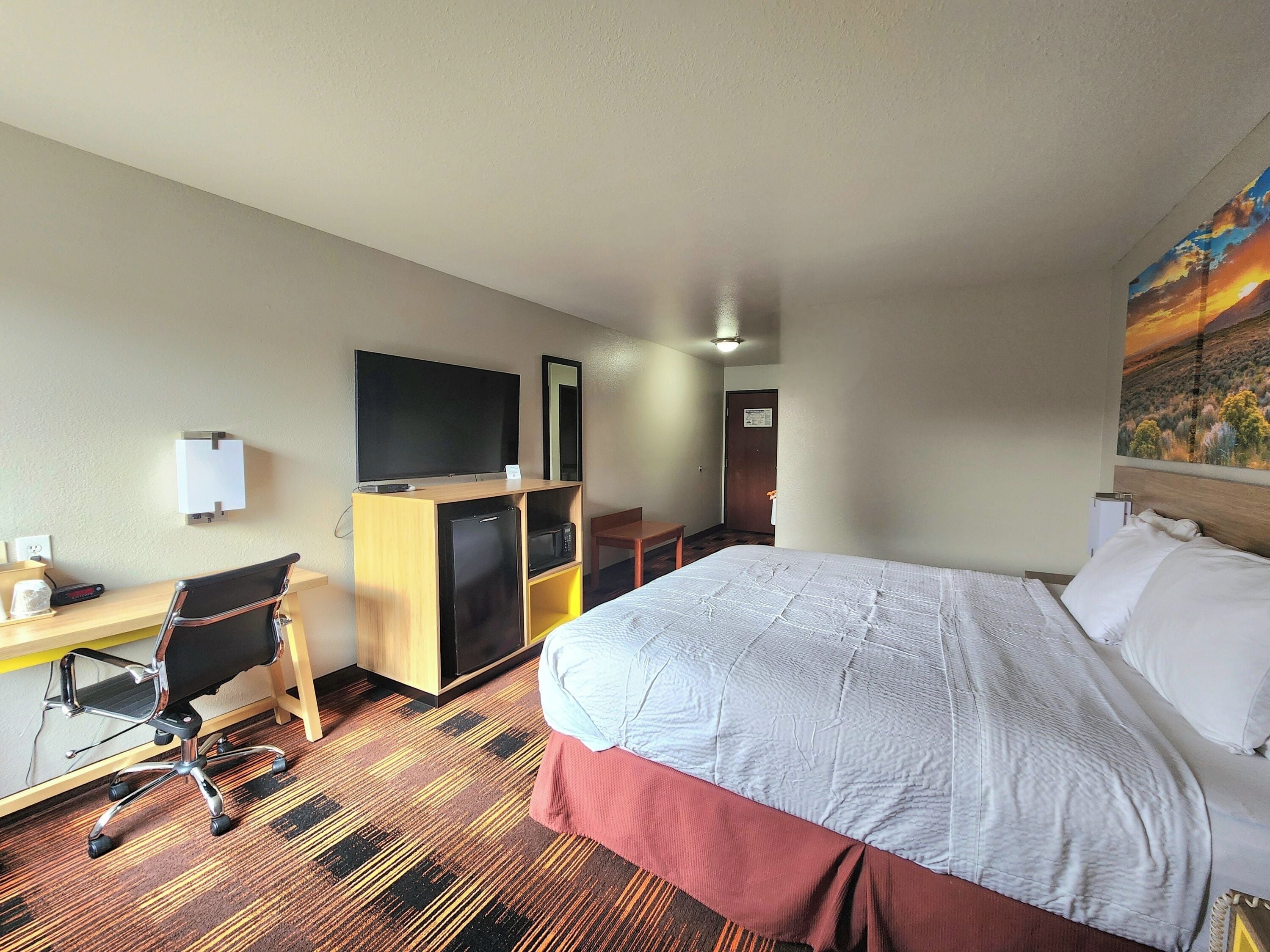 Habitación de hotel con cama, escritorio, silla, televisor y un cuadro en la pared.