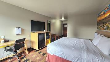 Habitación de hotel con cama, escritorio, silla, televisor y un cuadro en la pared.