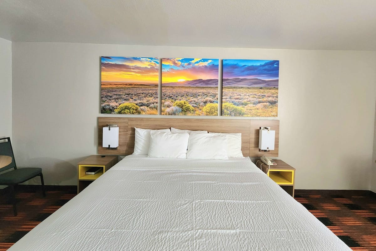 A hotel room with a large bed, white bedding, two bedside tables with lamps, and a wall-mounted painting of a desert landscape.