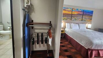 A hotel room with a bed, a painting of a sunset, a bathroom with a toilet and towel rack.
