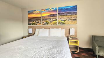 A hotel room with a large bed, a nightstand with a phone, and a chair.