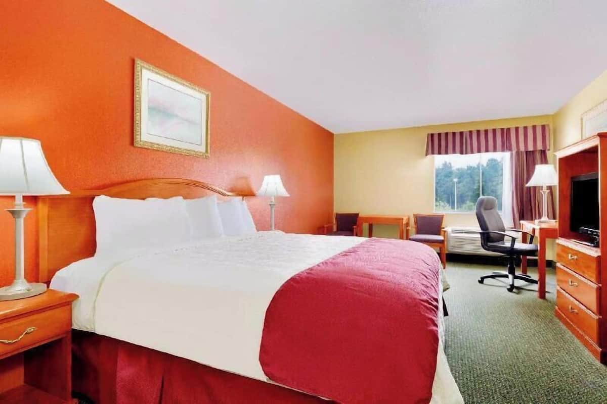 A hotel room with a large bed, two bedside tables with lamps, a desk with a chair, a television, and a window with curtains.