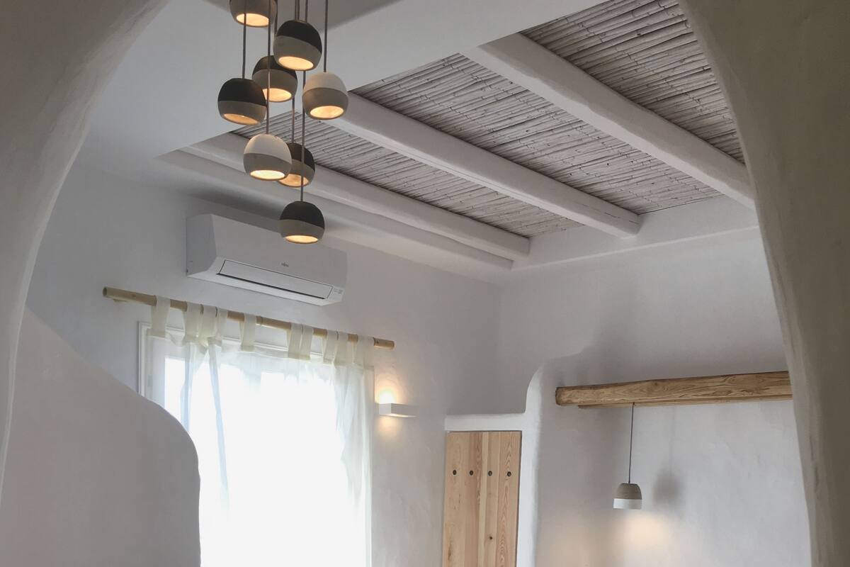 A modern bedroom with a large bed, a wooden wardrobe, a small seating area, and a ceiling with exposed beams.