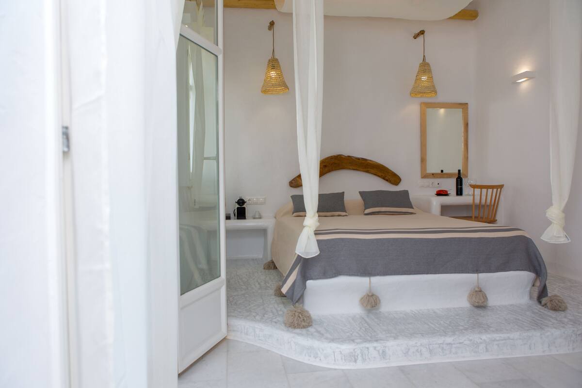 A bedroom with a bed, bedside tables, a nightstand, a chair, a mirror, and a hanging light fixture.