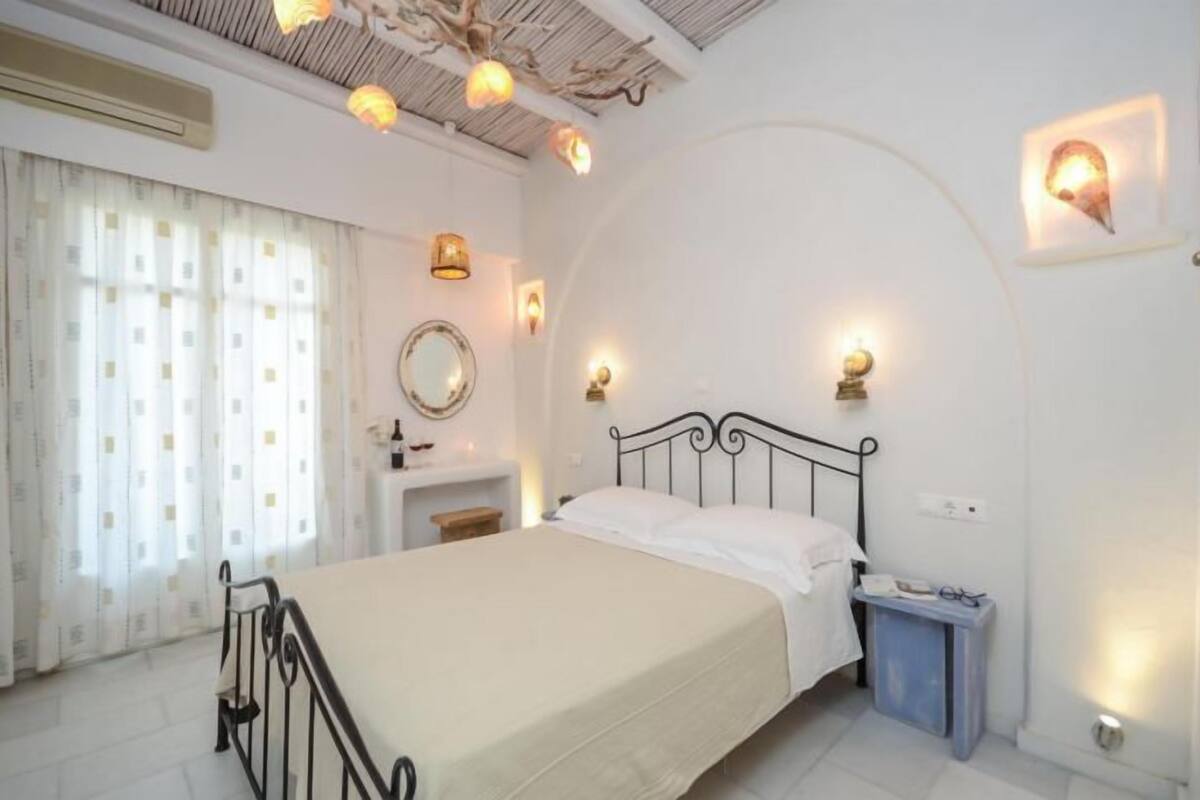 A bedroom with a bed, a bedside table, a mirror, and wall-mounted lights.