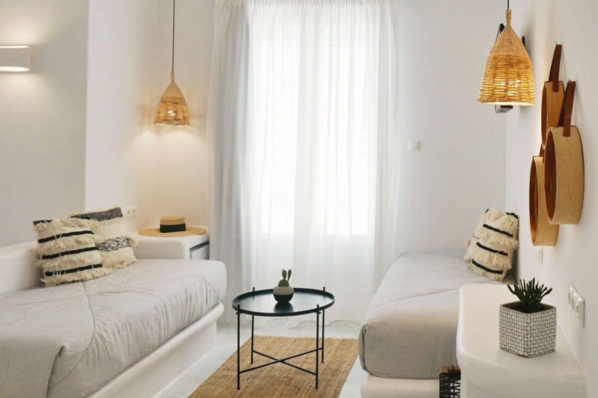 A minimalist bedroom with a bed, two bedside tables, a small round table, and a hanging light fixture.