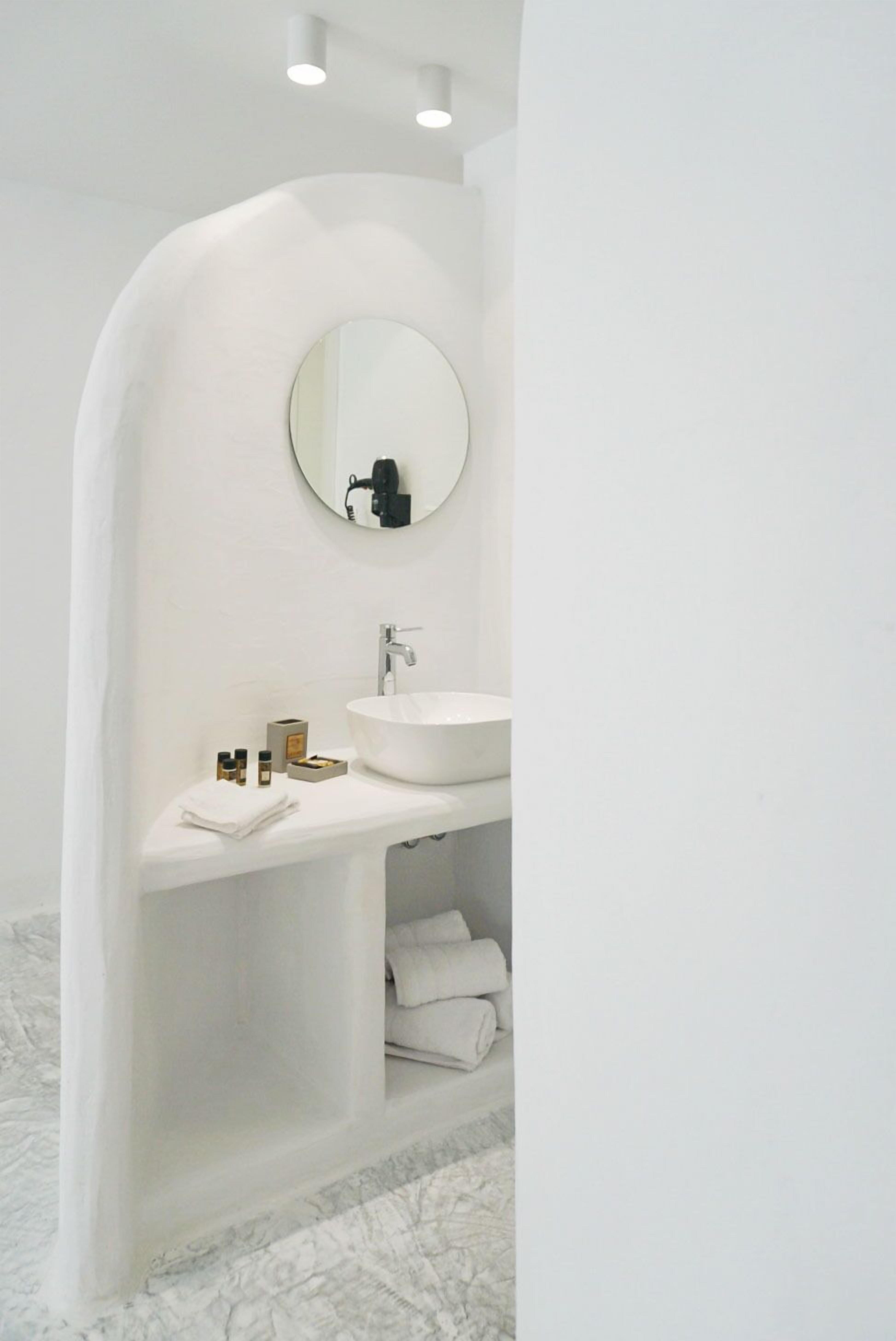 Een moderne badkamer met een wit wastafelmeubel, een ronde spiegel en een inbouwkastje met handdoeken en toiletartikelen.