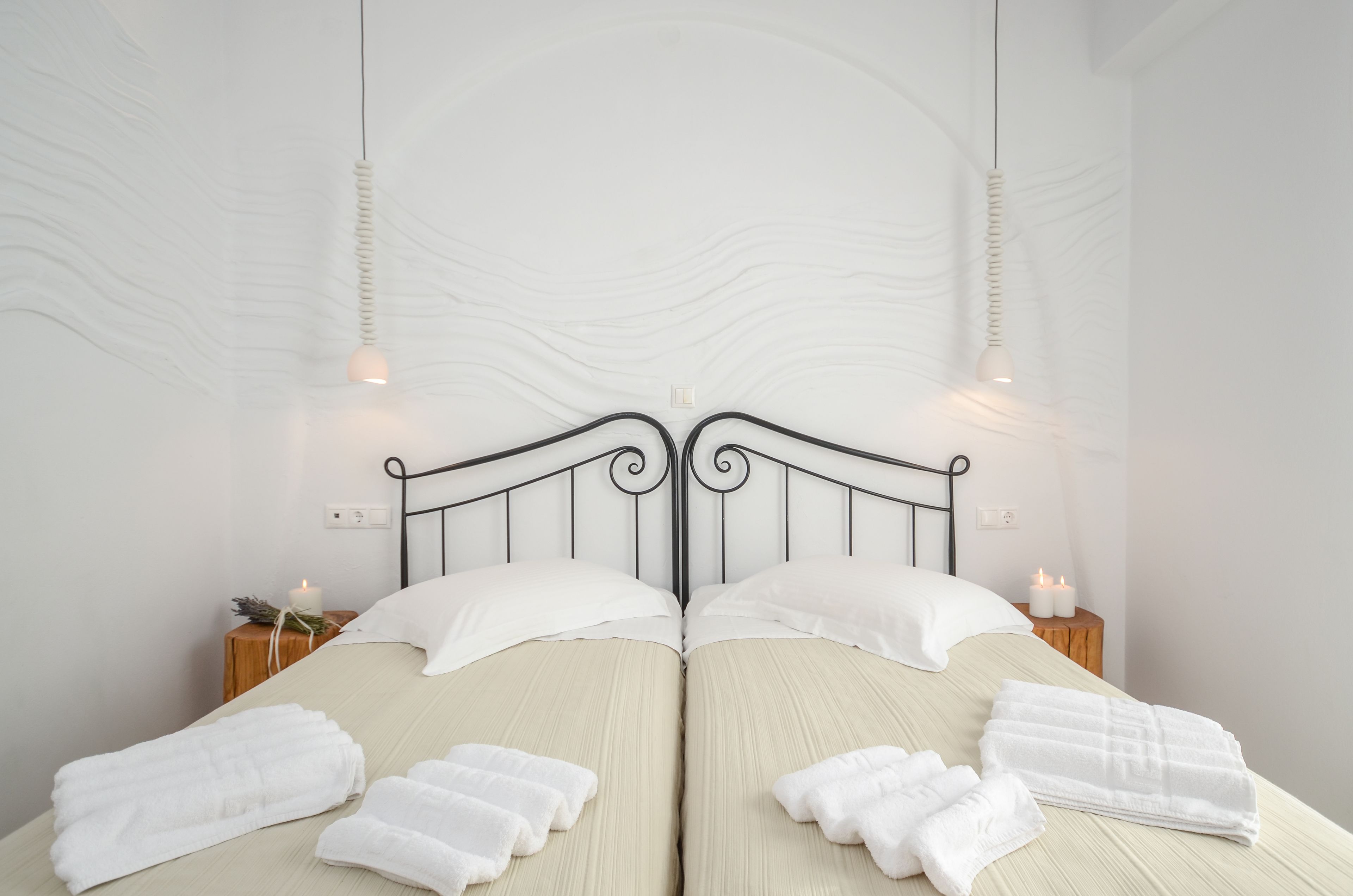 Una cama doble con ropa de cama blanca, un cabecero de metal negro y dos mesitas de noche con velas.