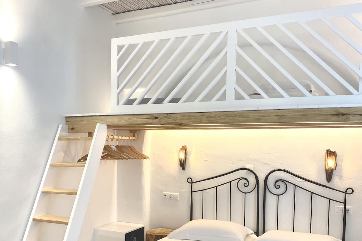 A bedroom with a bed, a wooden ladder, and a slanted ceiling.