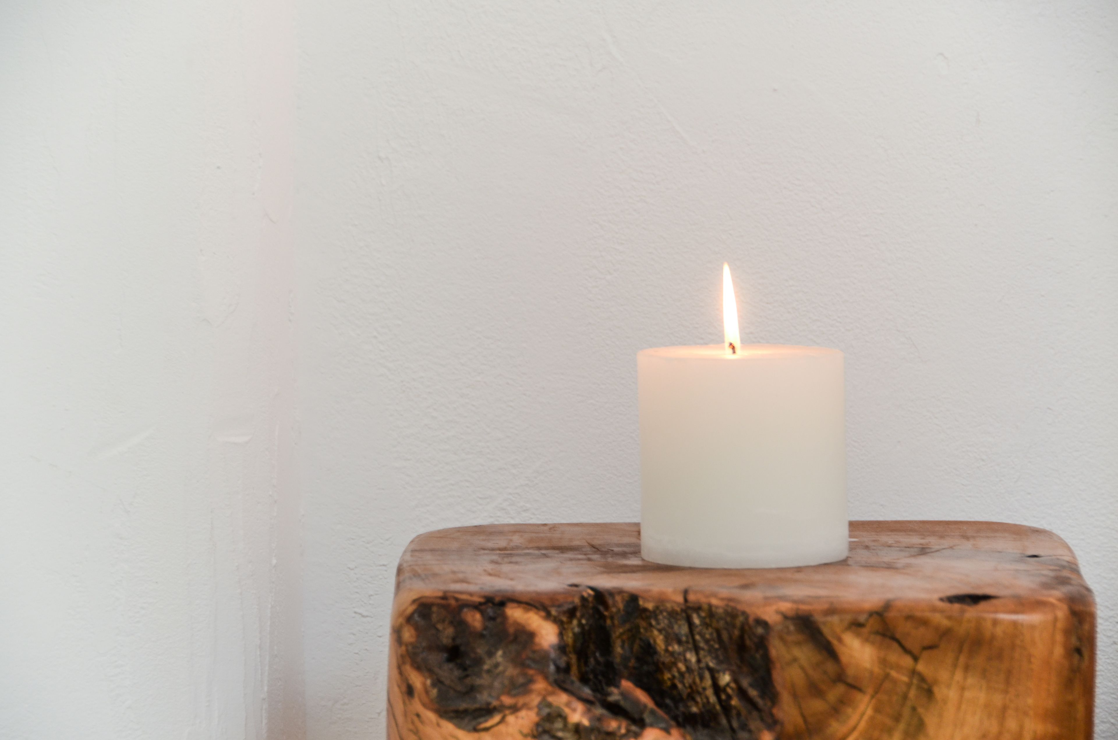 Una vela blanca sobre un tocón de madera frente a una pared lisa.