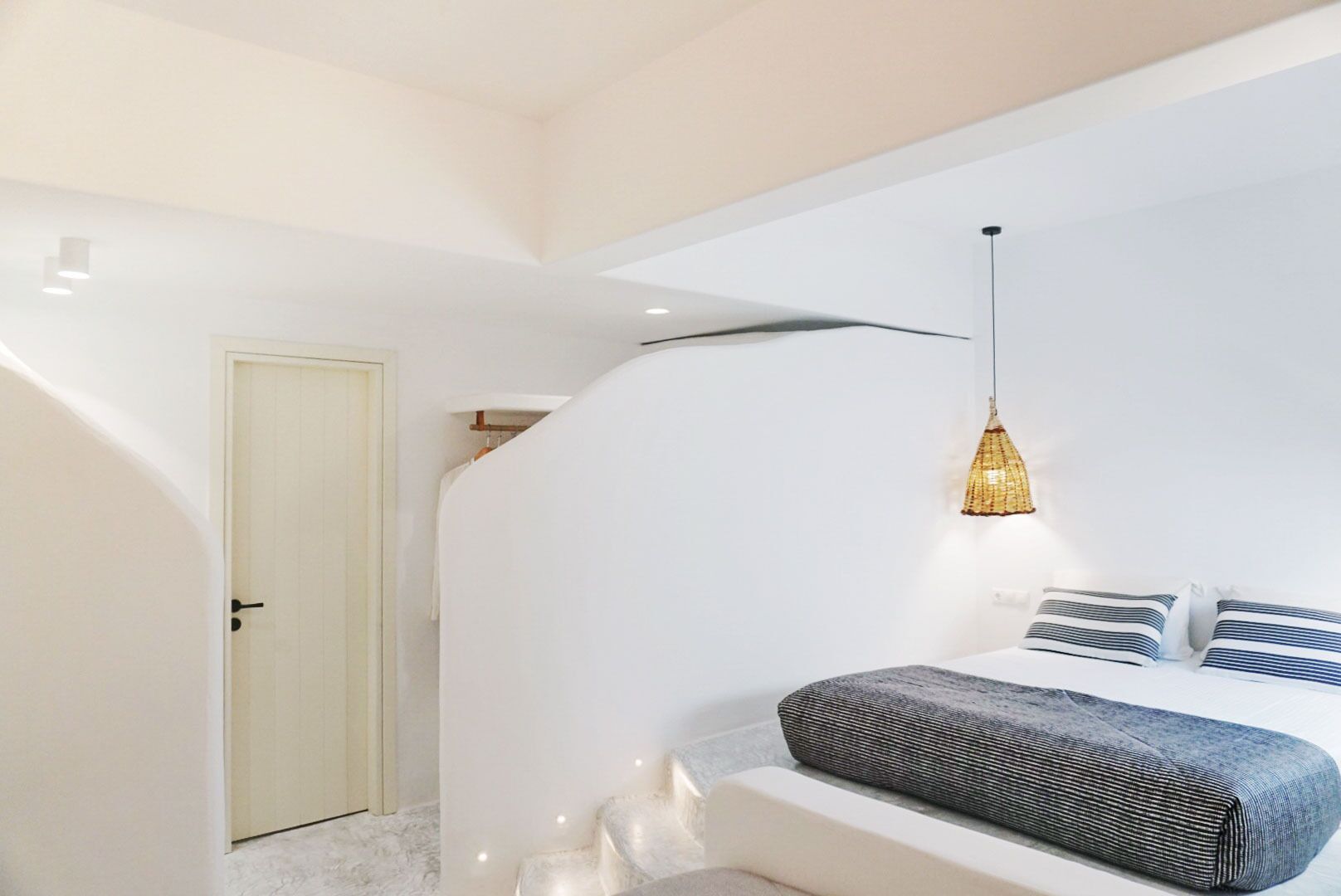 Et moderne soveværelse med hvid væg, en seng med stribede puder og en hængende lampe.