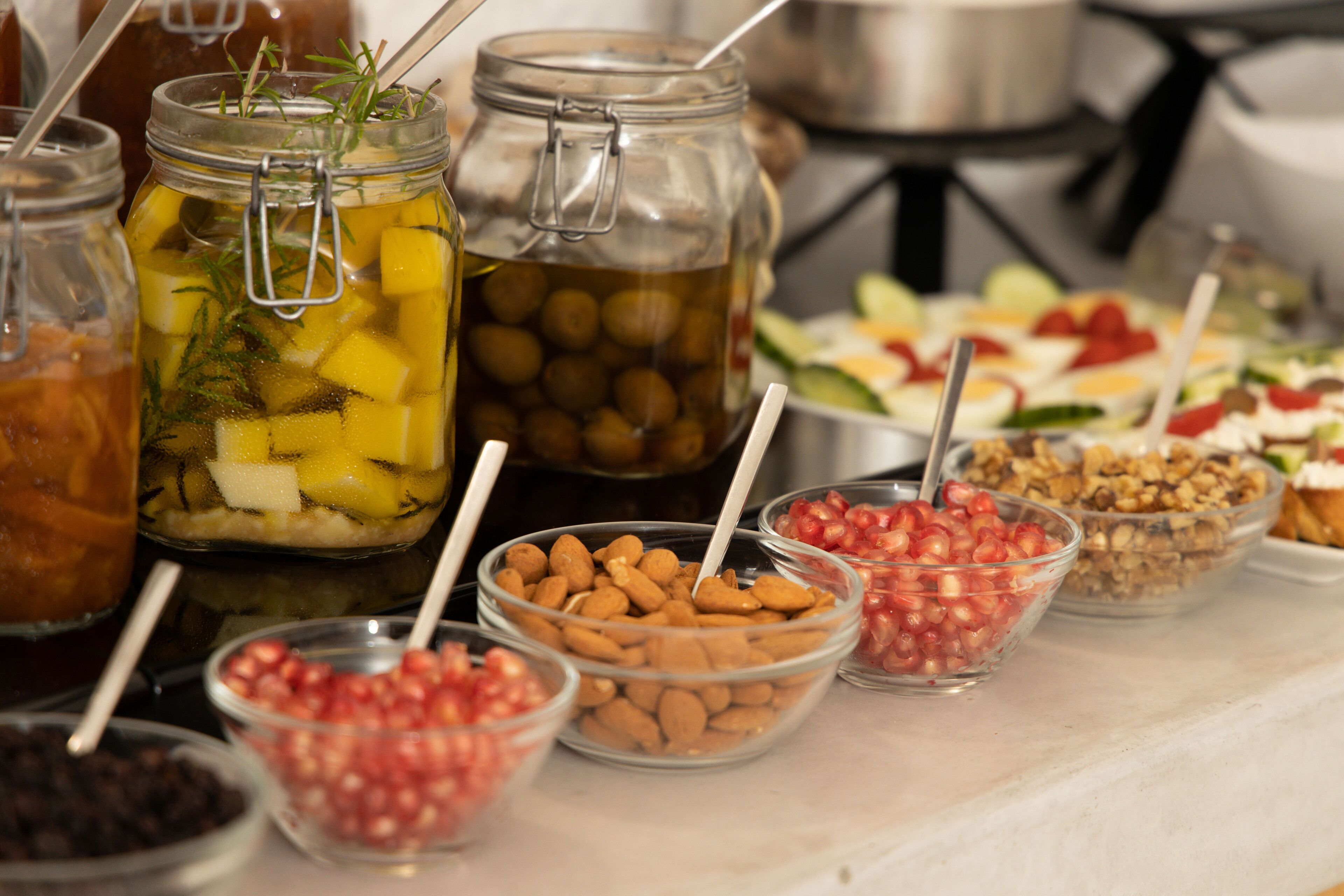 A buffet table with various food items including jars of pickled fruits, bowls of nuts, and fresh vegetables.