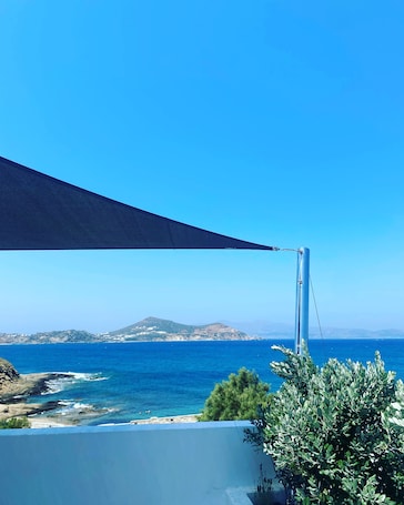 A seaside view with a clear blue sky, a rocky coastline, and a distant mountain range.
