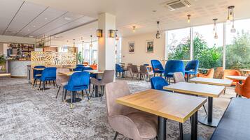 Un café moderne doté de plusieurs espaces de détente, notamment des tables et des chaises, ainsi qu’un bar avec un comptoir.