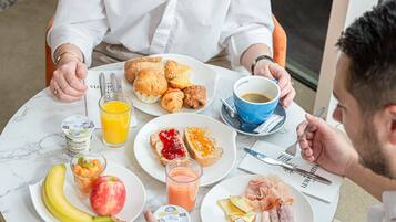 Una mesa redonda con alimentos para el desayuno, incluyendo cruasanes, tostadas, fruta y una taza de café.