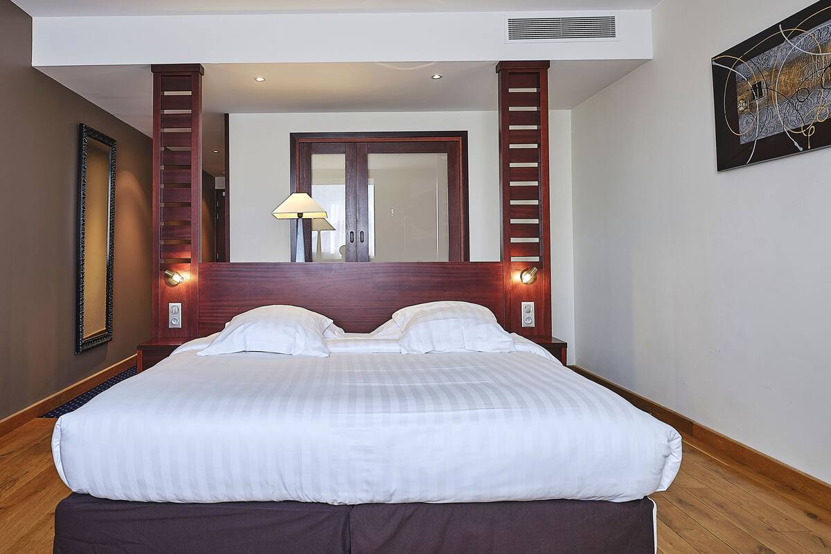A hotel room with a large bed, wooden headboard, a mirror, and a wall-mounted artwork.