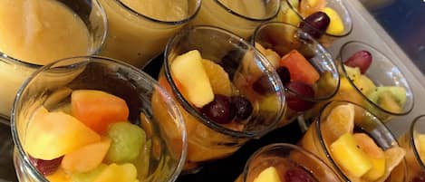 Une présentation de desserts dans des verres transparents, comprenant des puddings garnis de fruits et une variété de fruits.