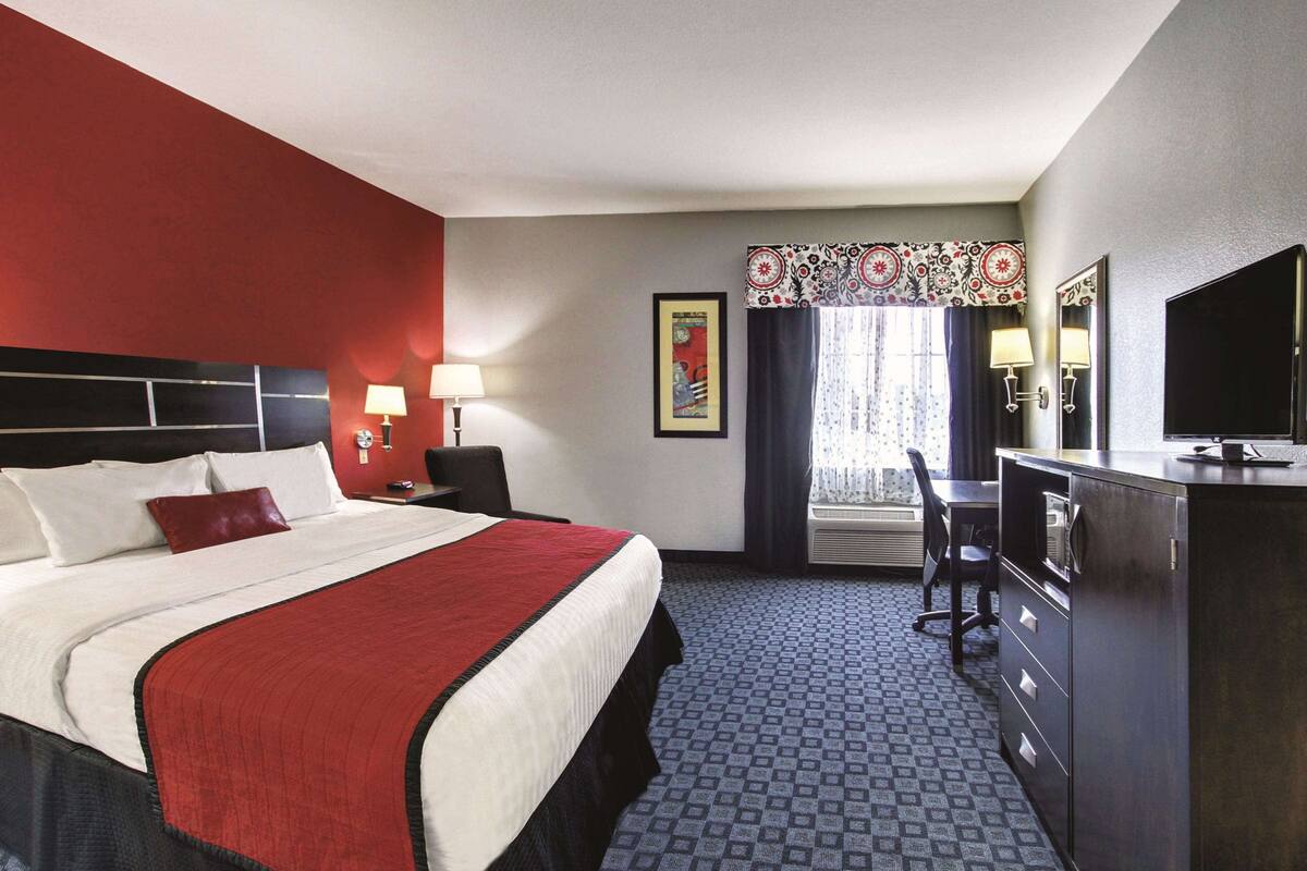 Habitación de hotel con una cama grande, un escritorio, un televisor y una ventana con cortinas.