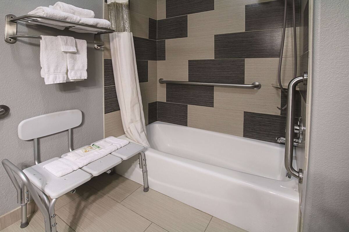 Un baño con bañera, ducha con cortina, toallero y un banco con toallas.