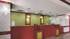 A reception area with a red and green color scheme, a counter with a cash register, and a sign indicating a manager on duty.