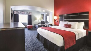 A hotel room with a large bed, a desk, a chair, and a small seating area.