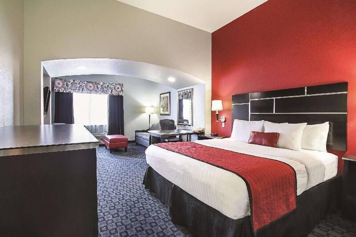 Habitación de hotel con cama, escritorio, silla, pared de acento roja y diseño de pared curva.
