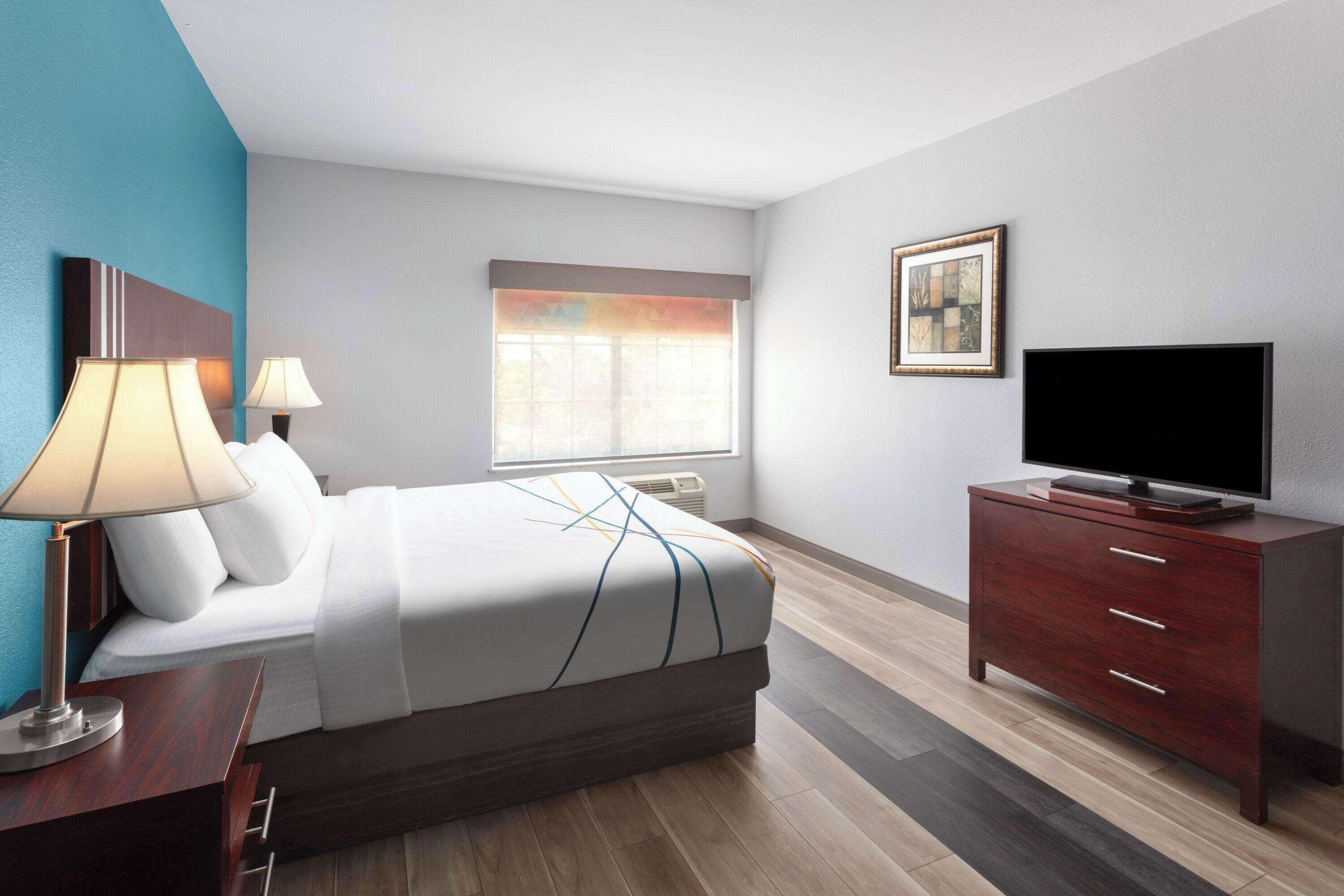 Een moderne hotelkamer met een bed, nachtlampjes, een televisie, een dressoir en een raam met zonwering.