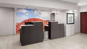 A reception area with a desert mural, three dark wooden counters, and a patterned trash bin. - La Quinta Inn & Suites by Wyndham Woodward (Woodward)