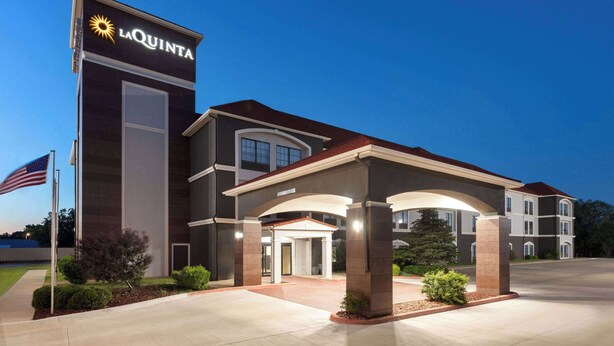 A La Quinta hotel with a modern design, featuring a prominent entrance with a covered walkway and a flagpole with an American flag. - La Quinta Inn & Suites by Wyndham Woodward (Woodward)
