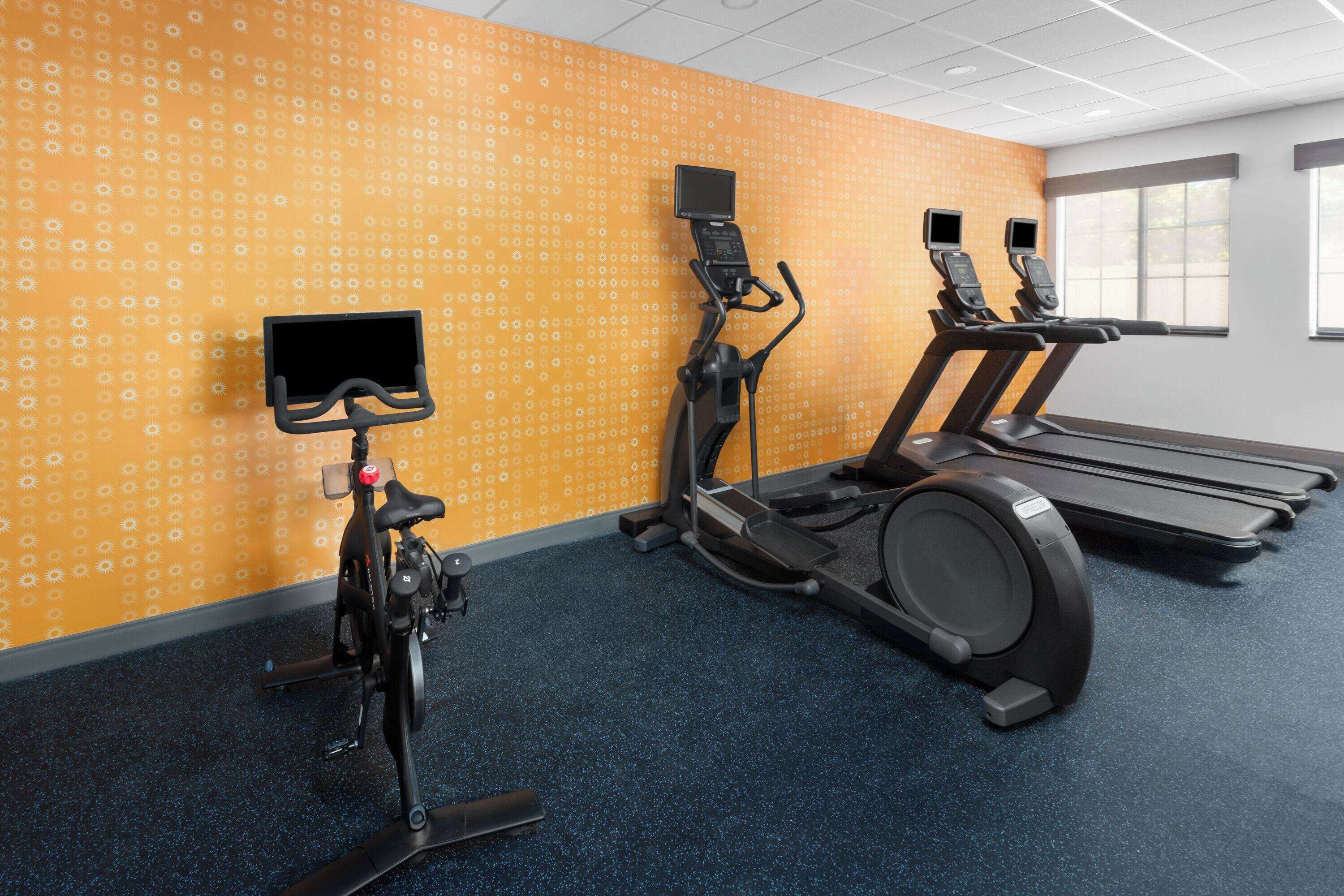 Un gimnasio con bicicletas estáticas, cintas de correr y una pantalla instalada en la pared.