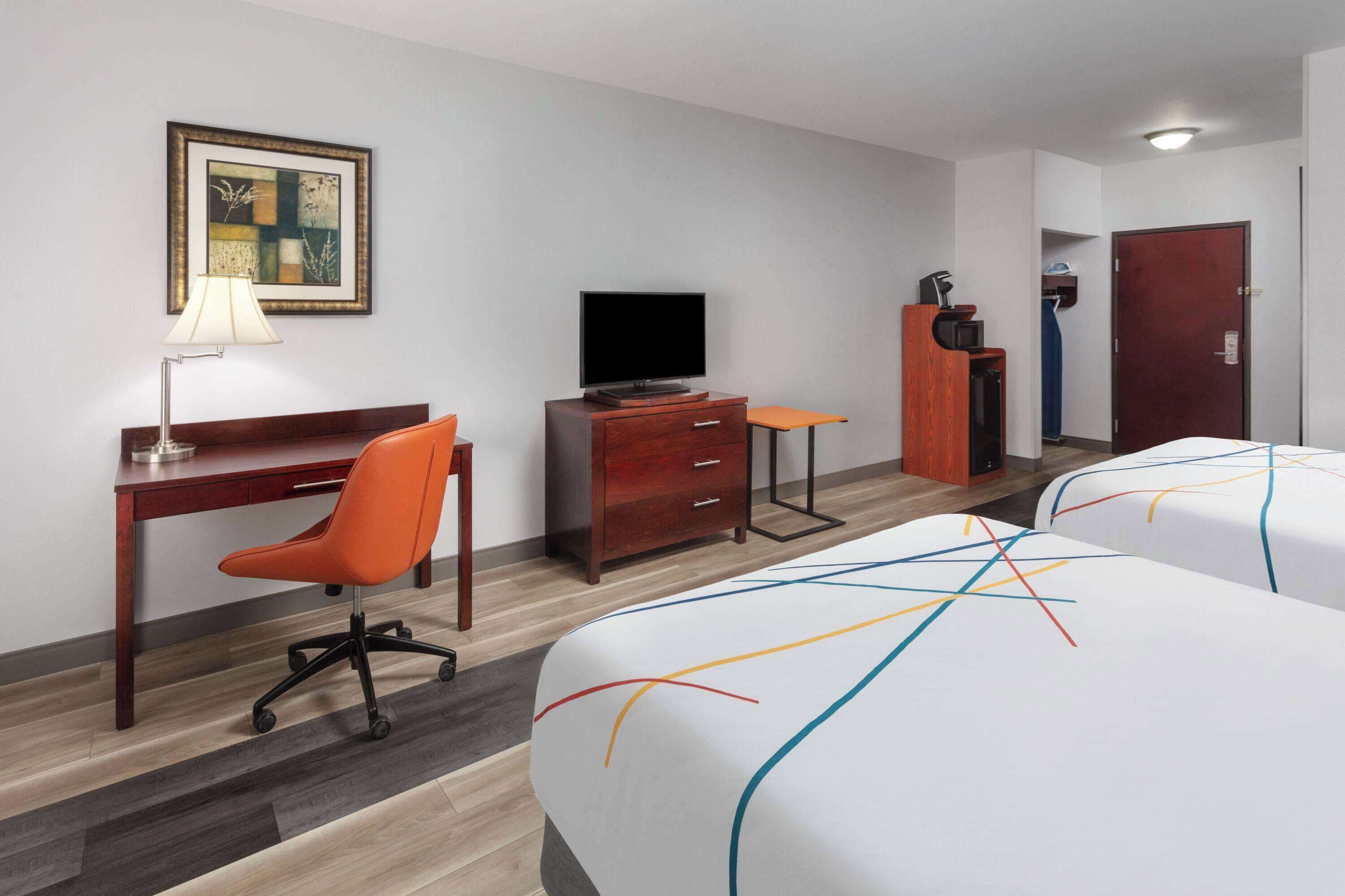 A hotel room with a desk, a television, a dresser, a bed, and a door.